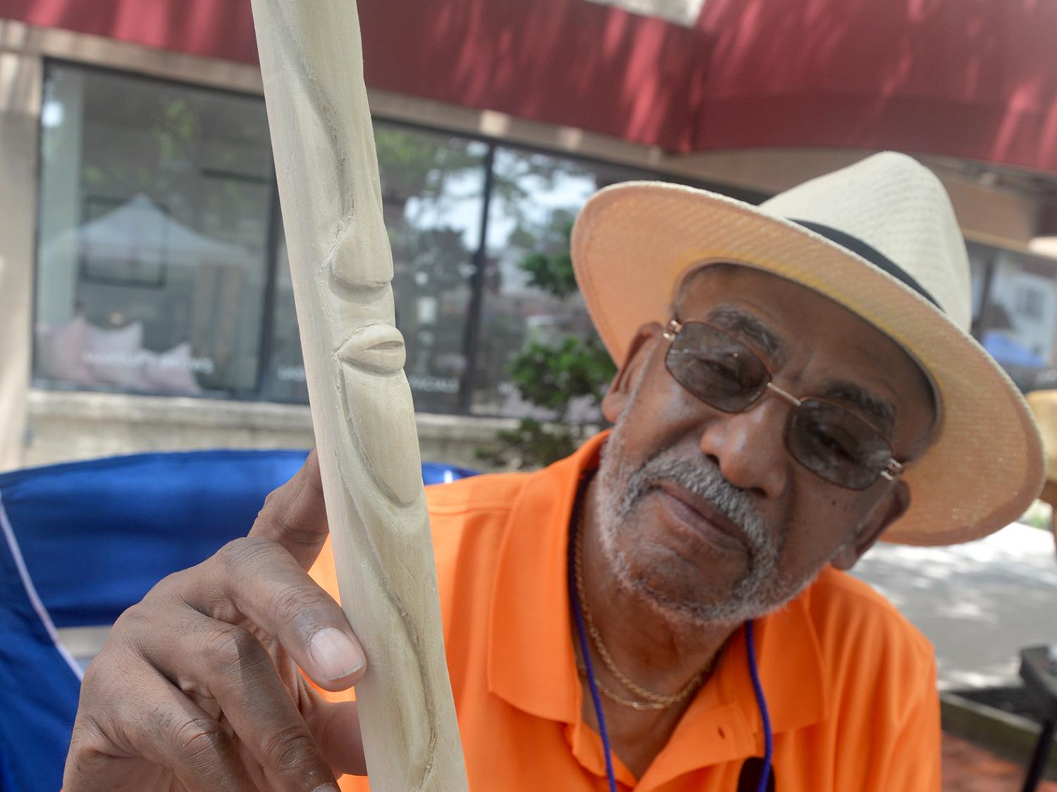 A person shows a wooden walking stick with carved faces on it