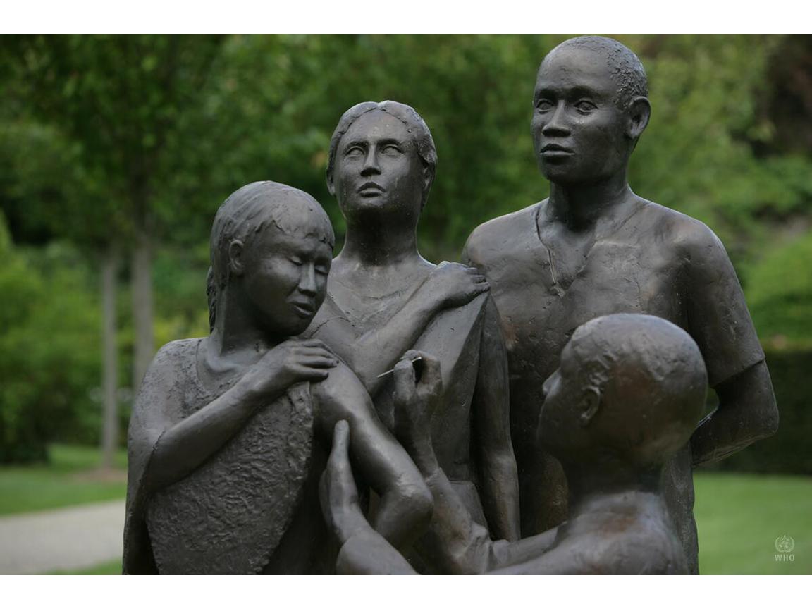Bronze statue of health worker giving vaccine to one person as two others look on.