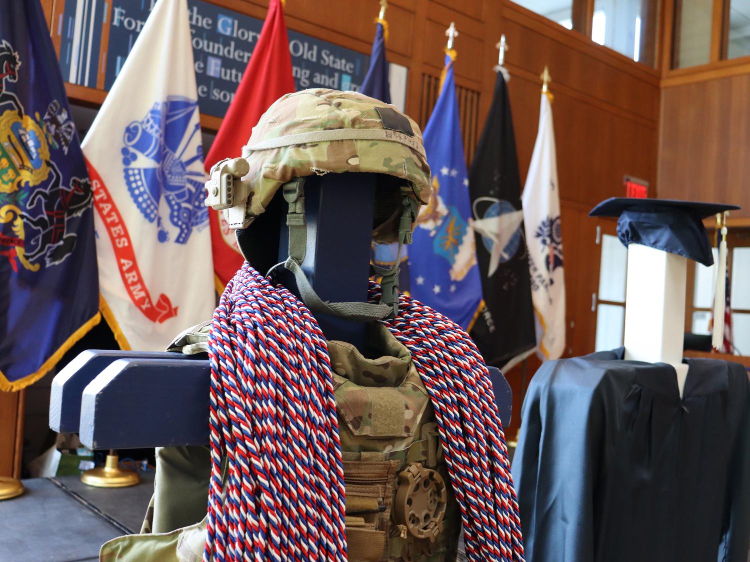 Red, white, and blue honor cords lay on the shoulder of camouflaged military combat gear.