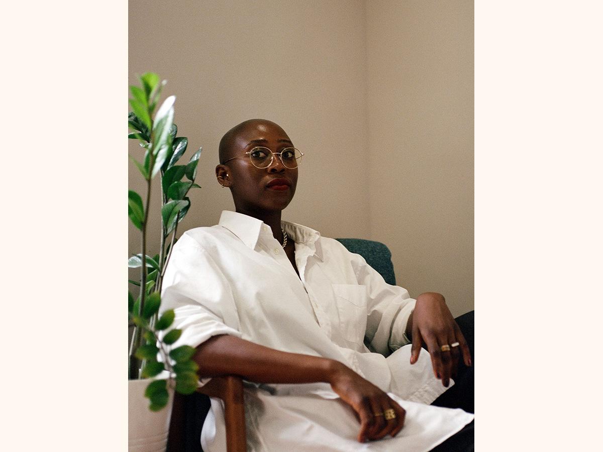 Critically acclaimed author Pemi Aguda sitting on a chair in front of a plant