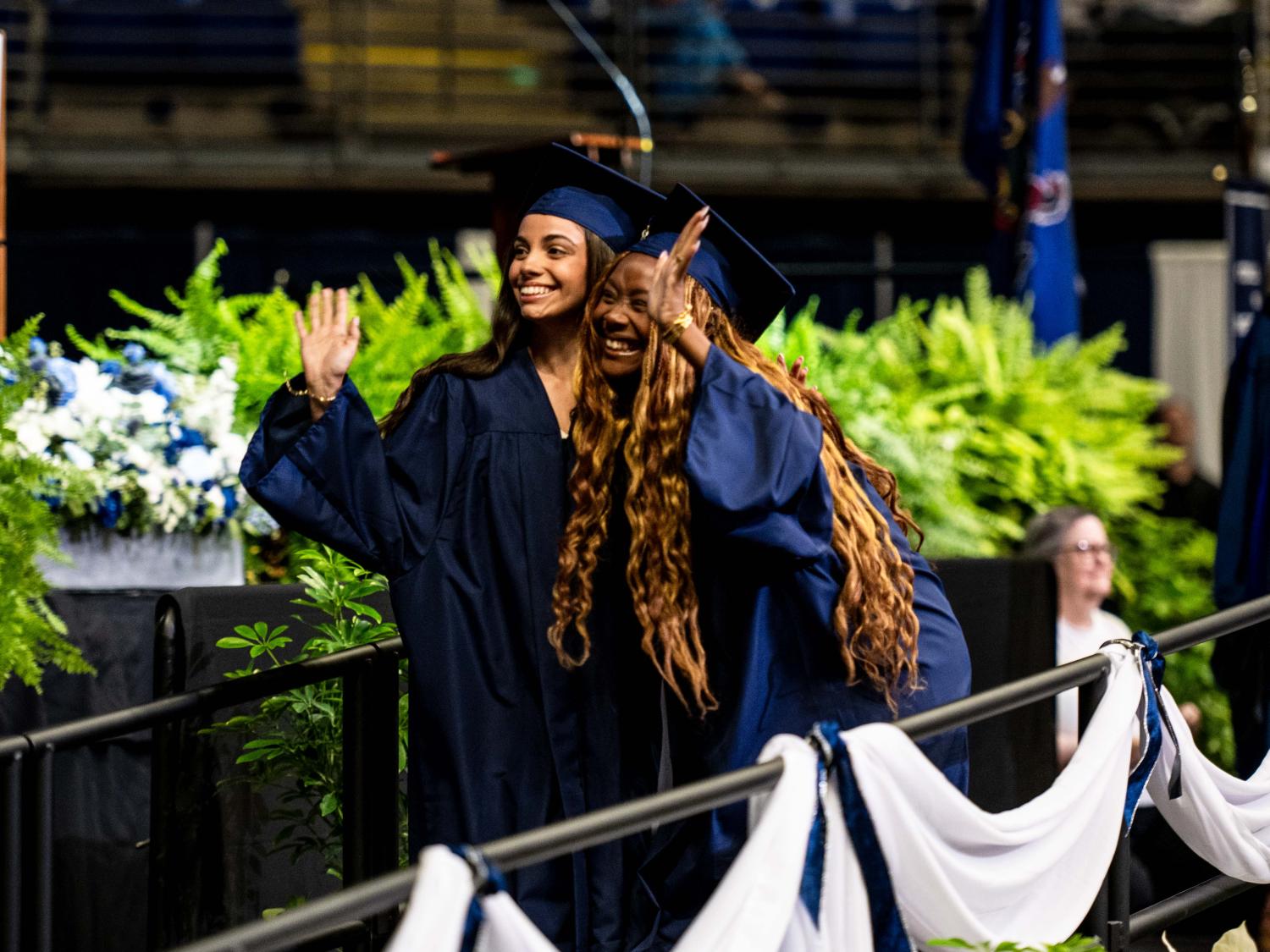 Graduates hugging each other and waving to the crowd