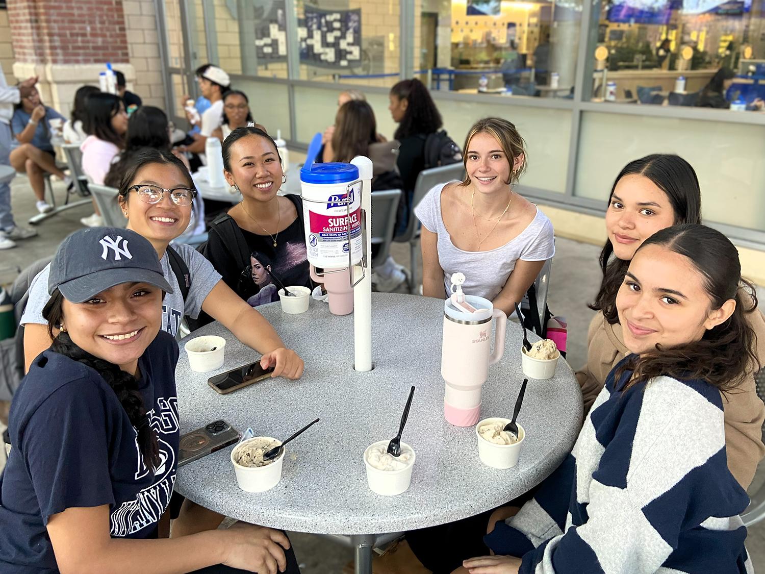 A group of young, female students sit around a circular table with cups of ice cream in front of them.