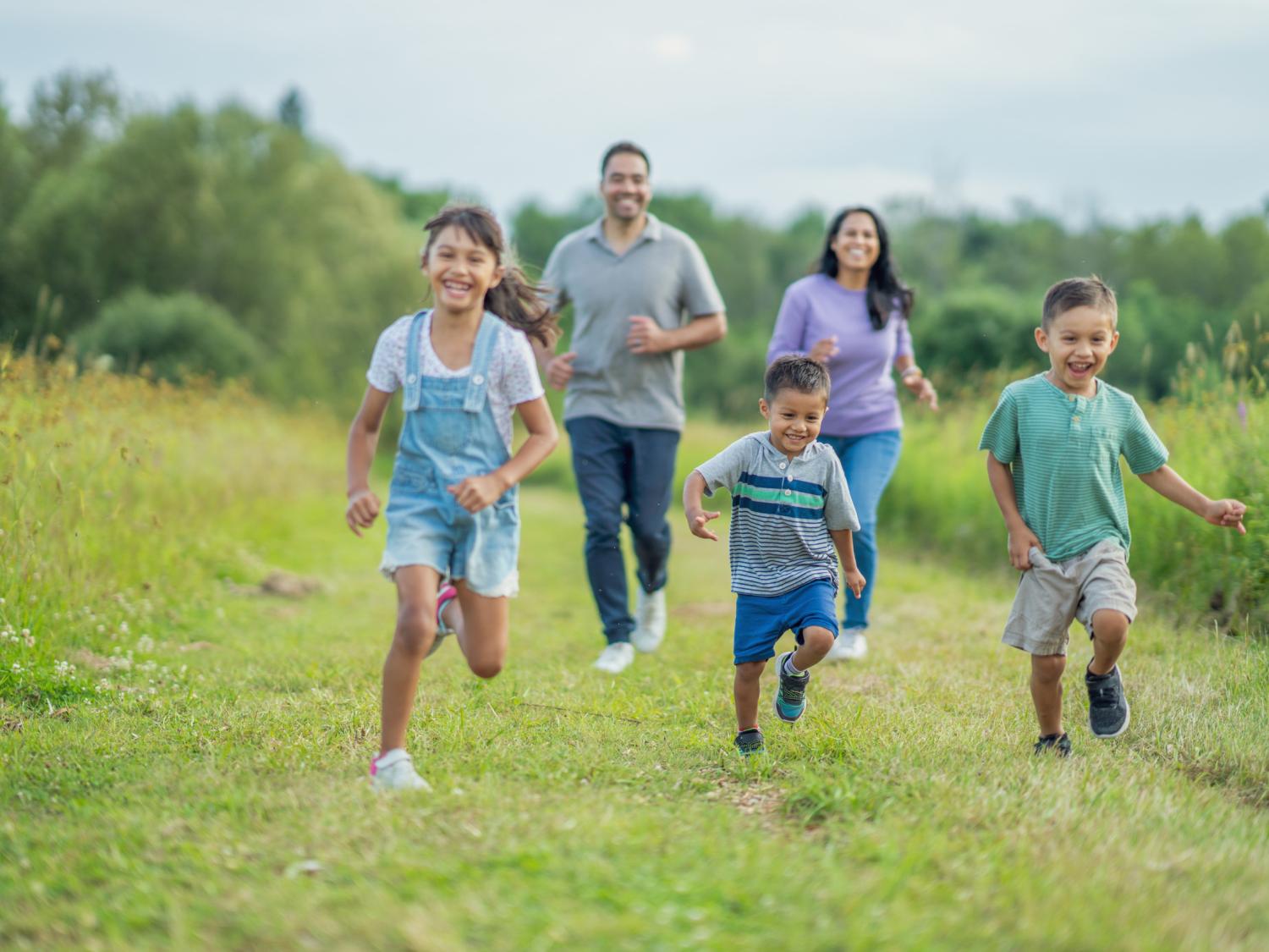 Three children and two parents running in grassy field