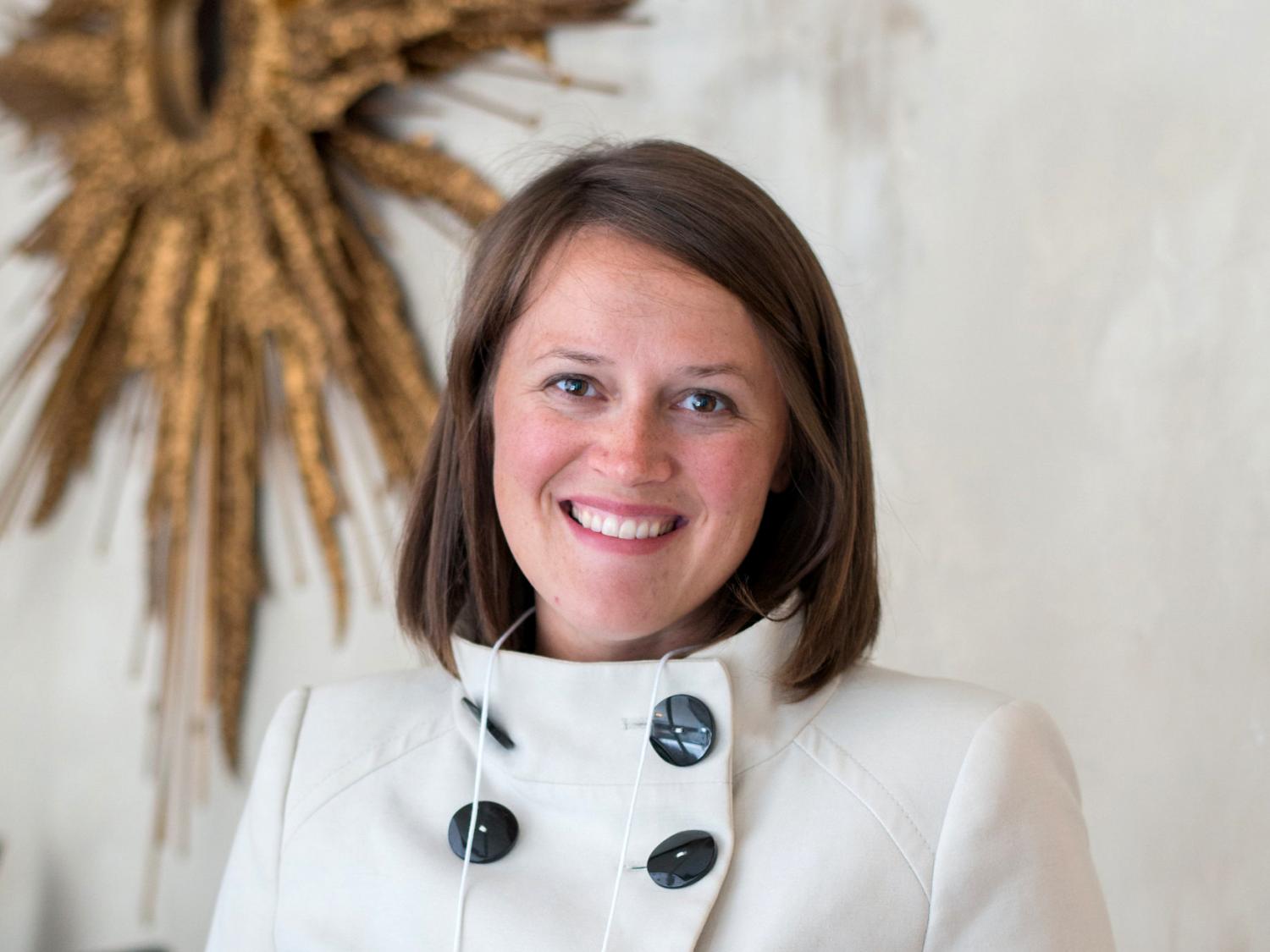 Headshot of Amanda Hellman with a piece of sunburst artwork on the wall behind 