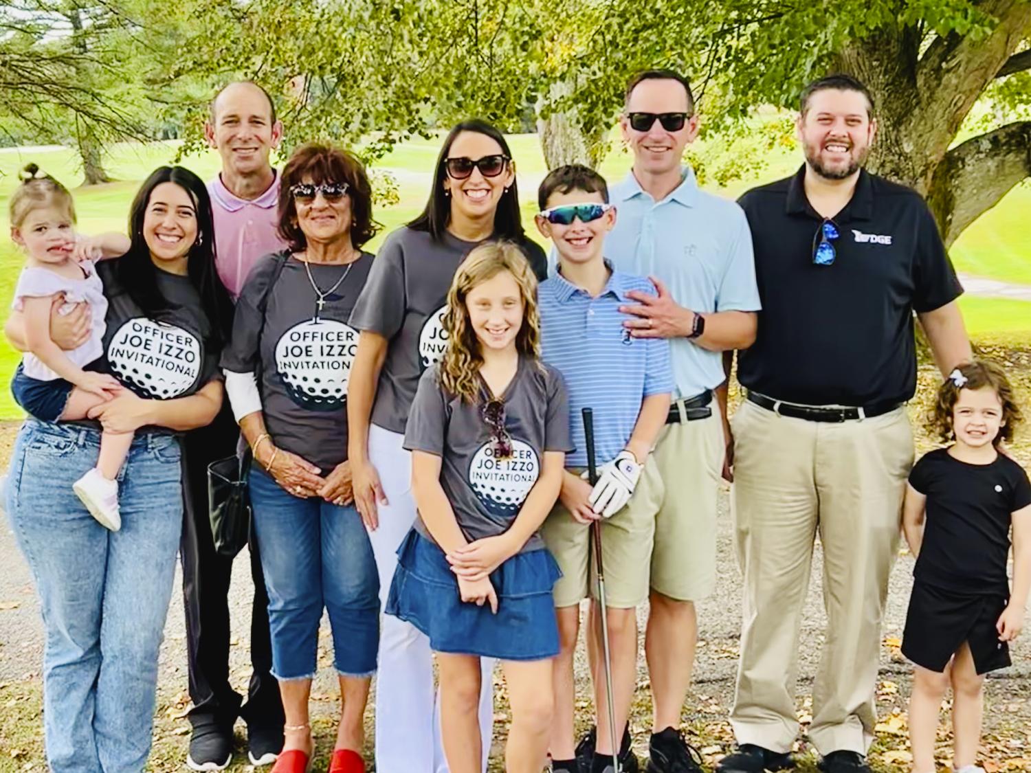 Family photo of ten people posing for a photo under a tree with a golf course in the background