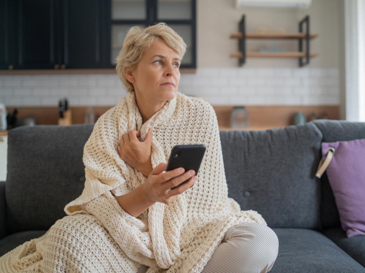 A person sits in their living room on a couch, with a blanket wrapped around them