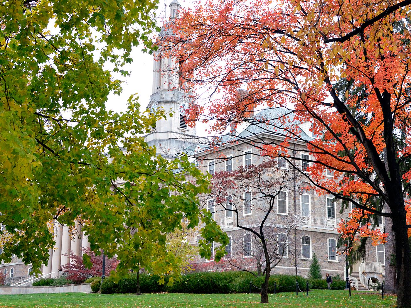 A picture of Old Main, an old stone building with trees on either side in orange and green colors.