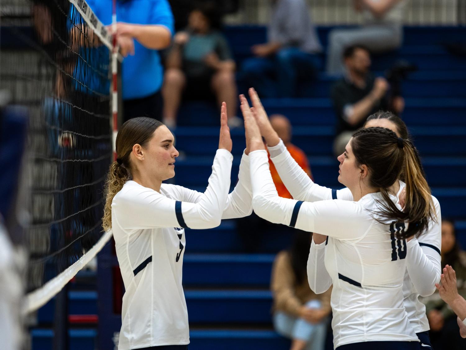 Two members of the Penn State Behrend women's volleyball team high-five after scoring a point.