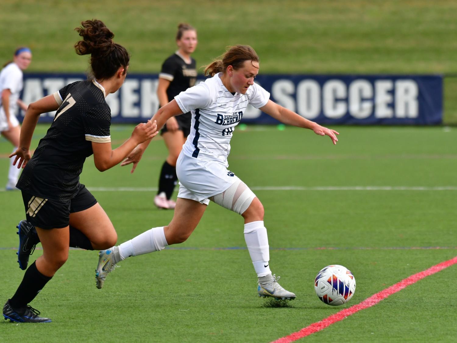A member of the Penn State Behrend women's soccer team advances the ball past a defender.