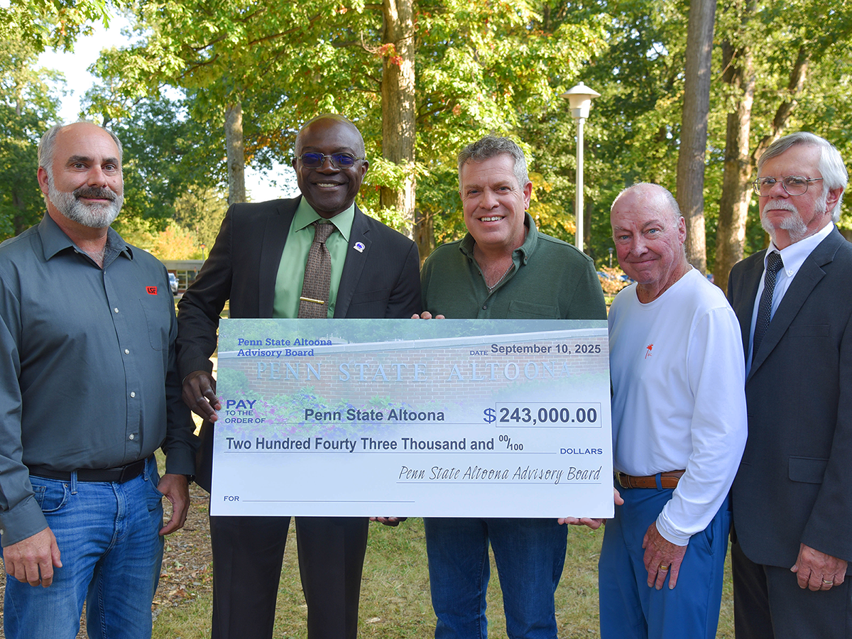 Five men stand outdoors holding a large ceremonial check for $243,000 presented to Penn State Altoona by its Advisory Board.