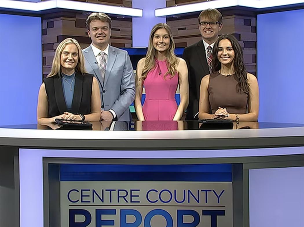 Five well-dressed students on a TV newscast set