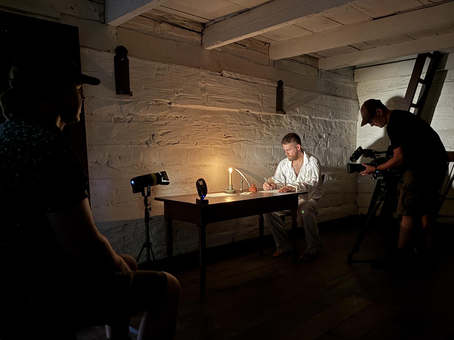 Person sitting at a desk in a dark room working by candlelight.