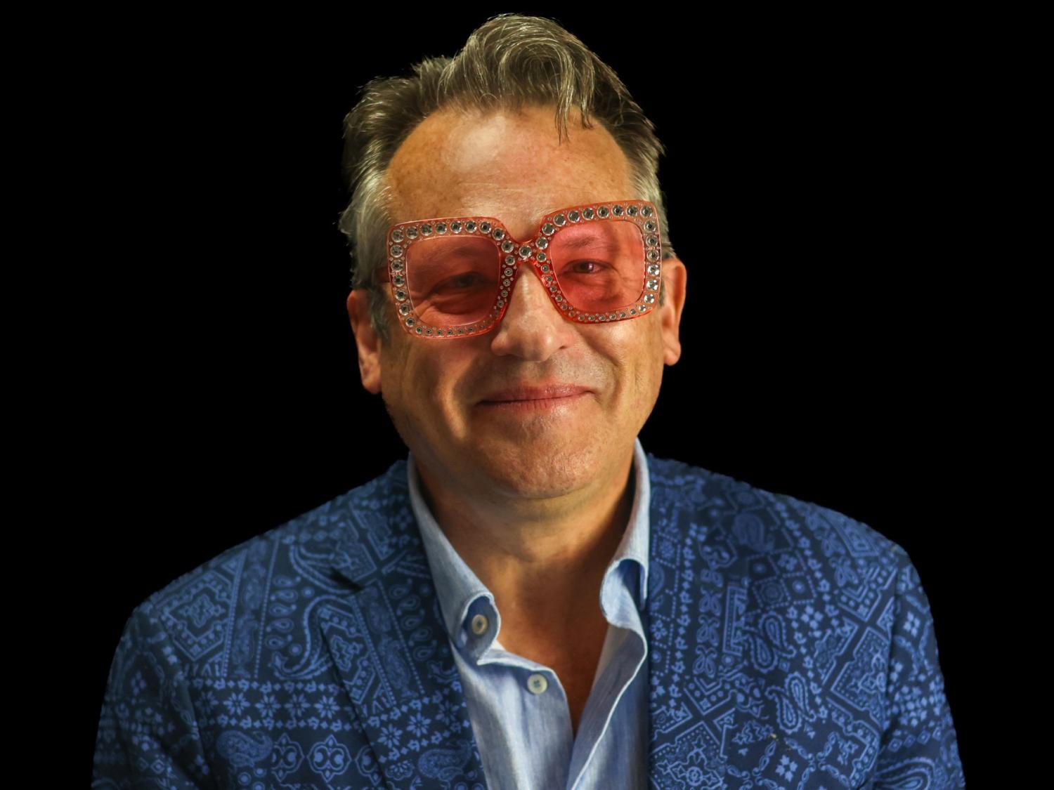 Matthew Restall wears a paisley blazer, blue shirt and Elton John-style pink glasses. 