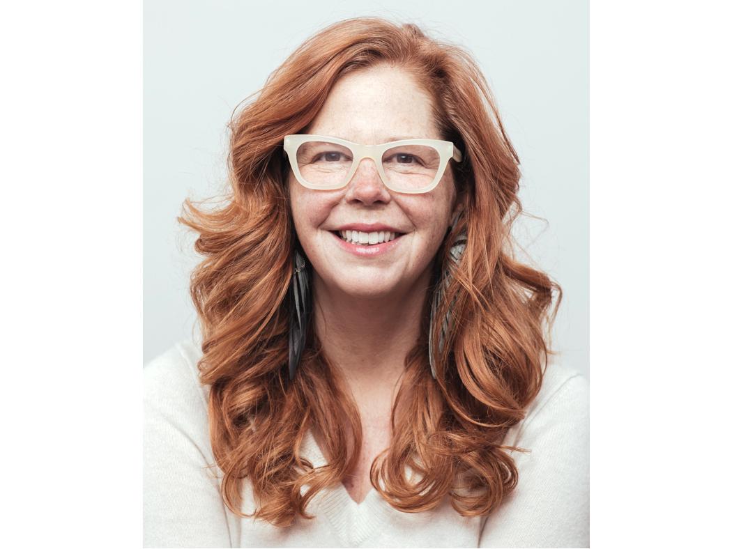 An individual with red hair and white-framed glasses against a white background.