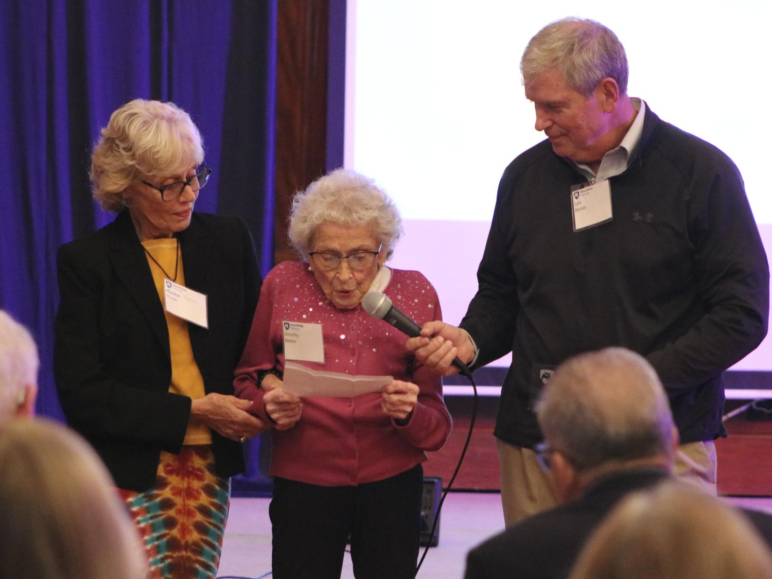 Dorothy Bieber holding papers and speaking into a microphone while being supported on both arms by her children.