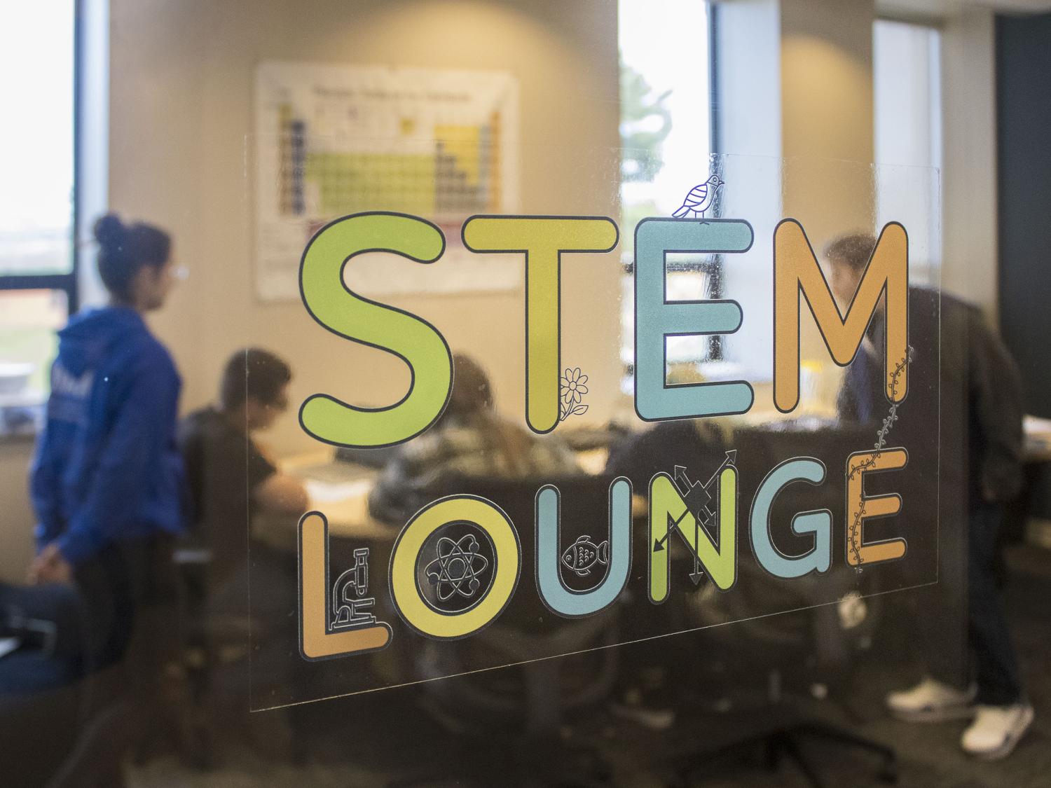A view through a glass window of students gathered inside the new STEM Lounge