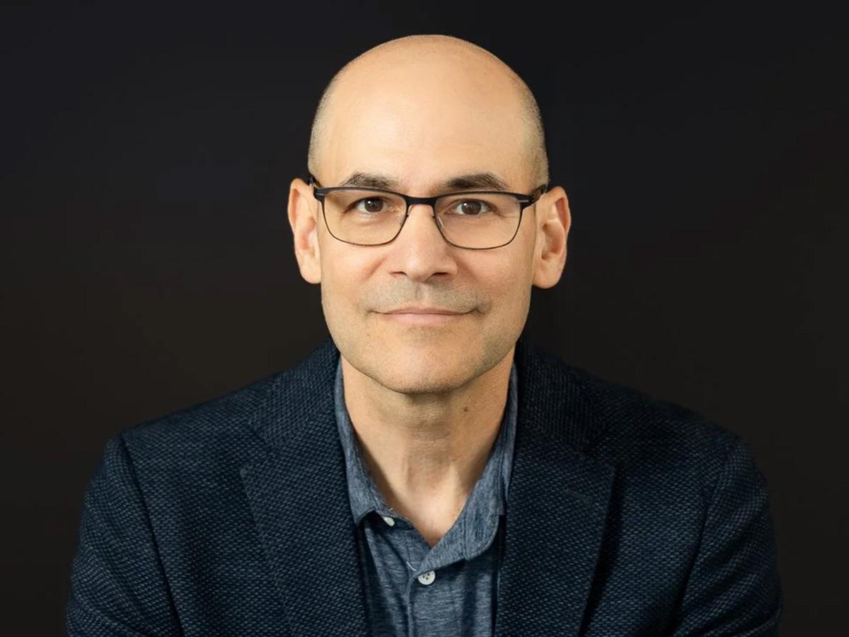 Benjamin DeAngelo is a bald man with glasses wearing a dark blazer and a blue shirt.