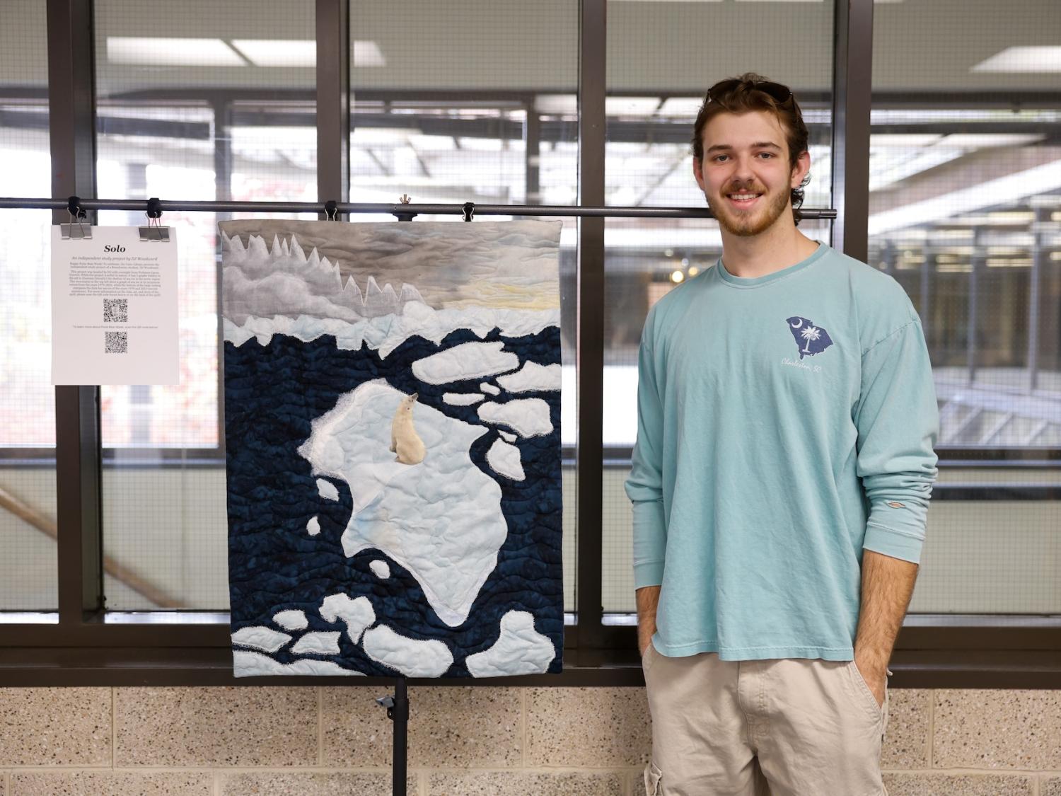 DJ Woodward standing next to his quilt with a polar bear on a sheet of ice