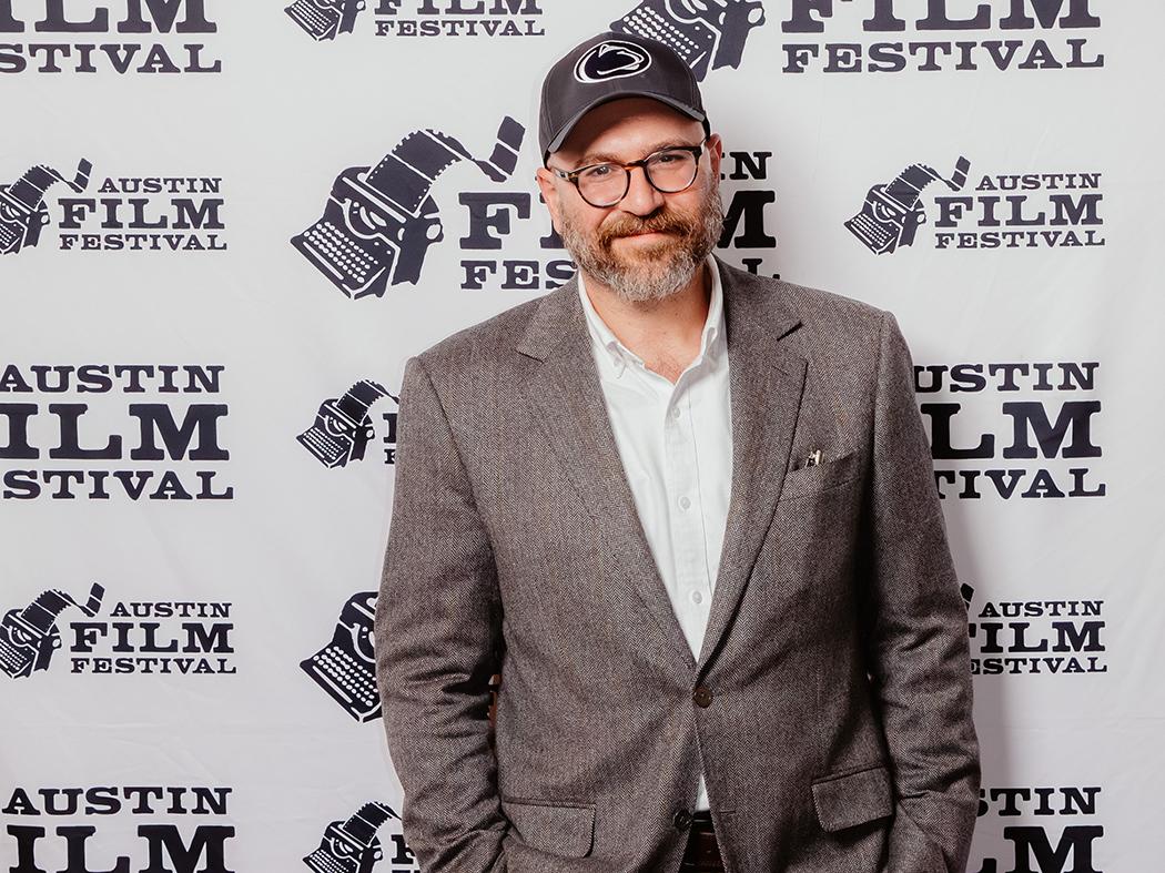 Bearded man in Penn State ballcap wearing a coat and collared shirt.