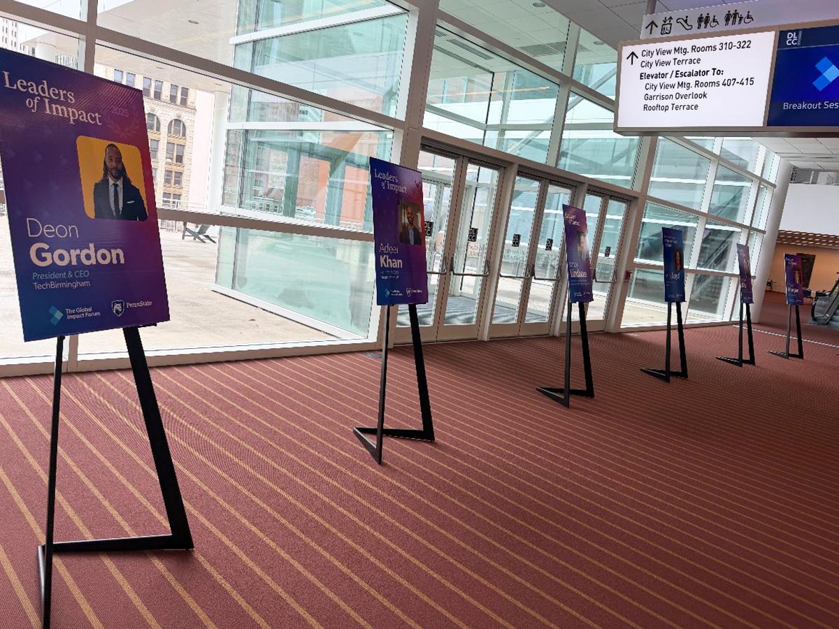 Colorful Leaders of Impact posters line a hallway at The Global Impact Forum, featuring speaker names and photos.