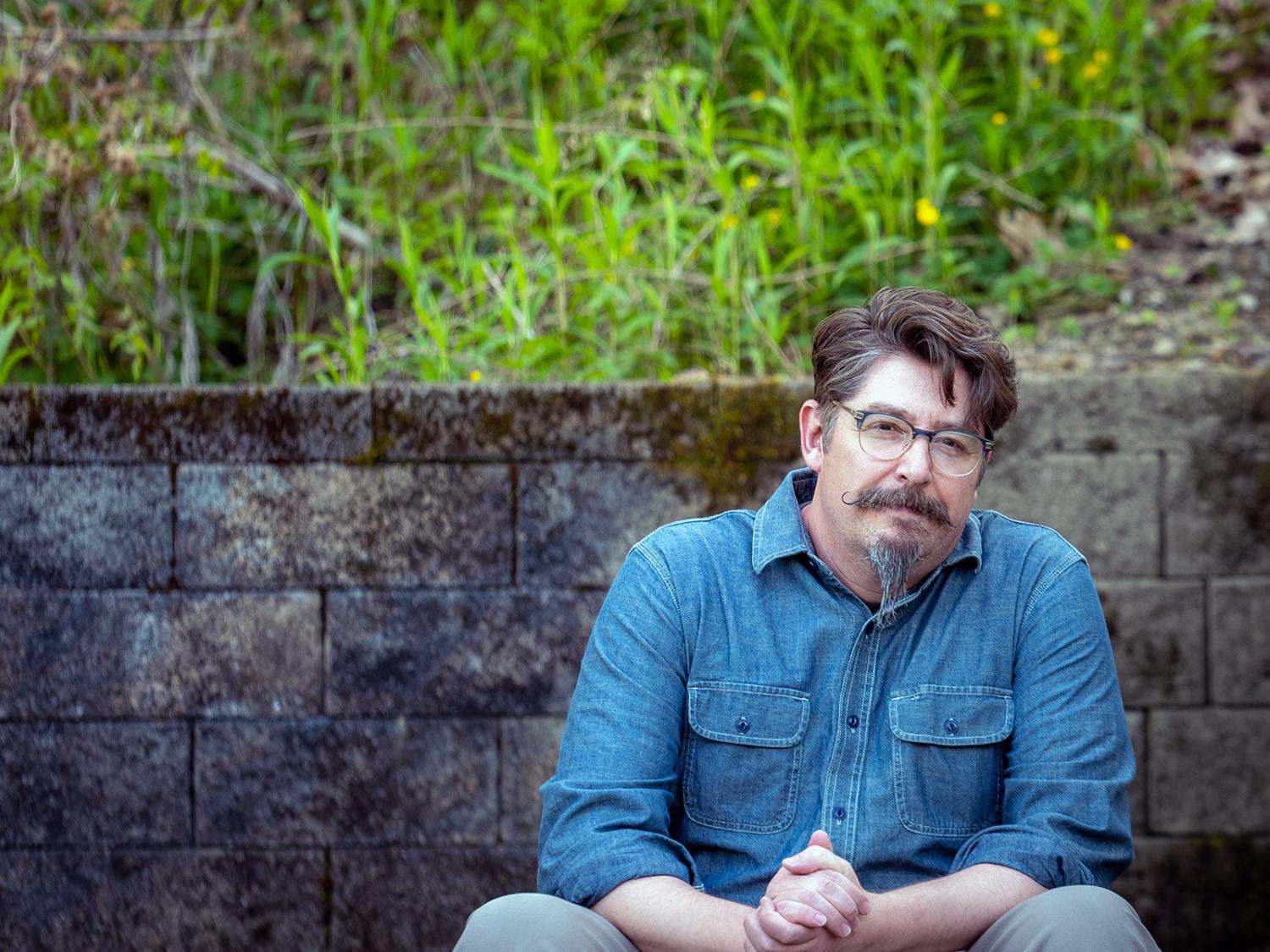 Matthew Ferrence sitting in front of cinderblock wall with grass in background
