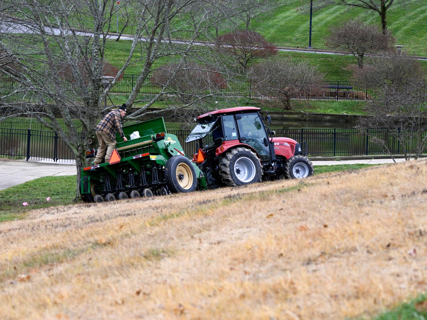 A large tractor pulls a seed spreader along an area of dead grass