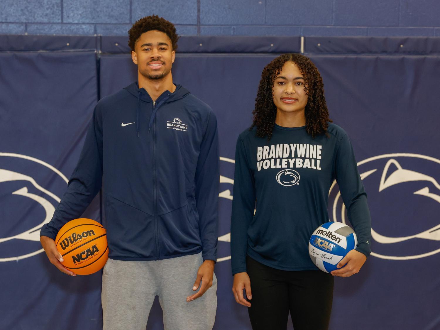 A male student holds a basketball and a female student holds a volleyball.