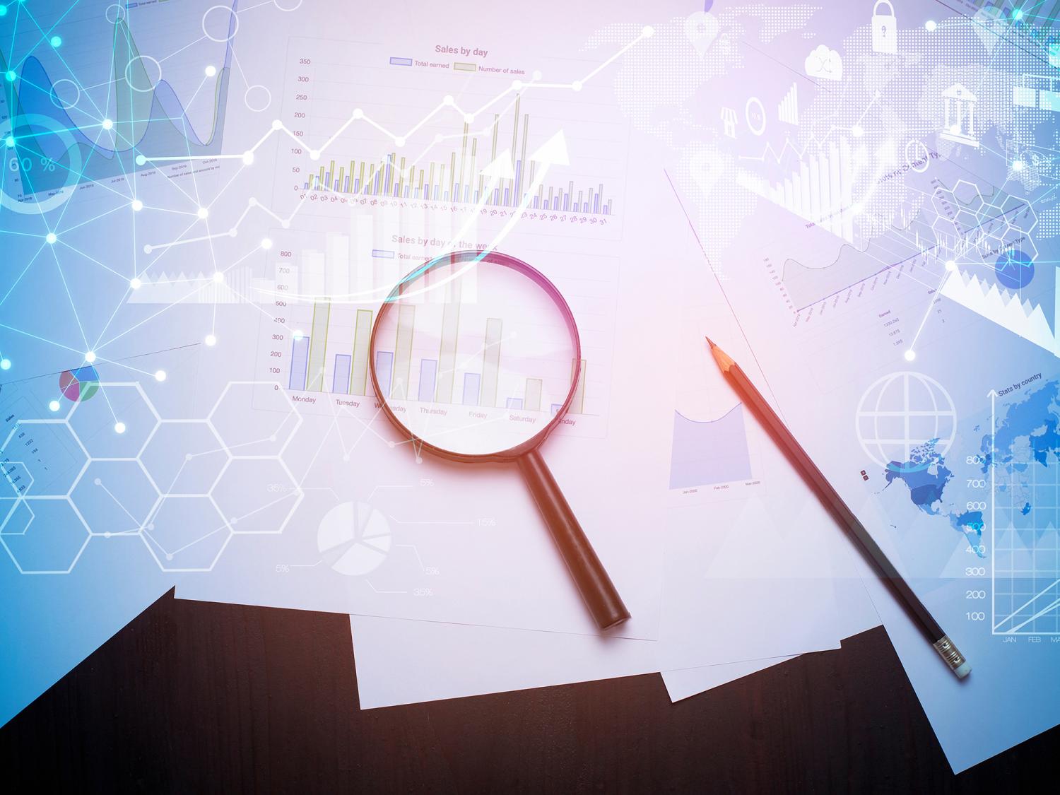 Magnifying glass and pencil on printed charts with digital overlays of graphs and maps representing global data and analytics.