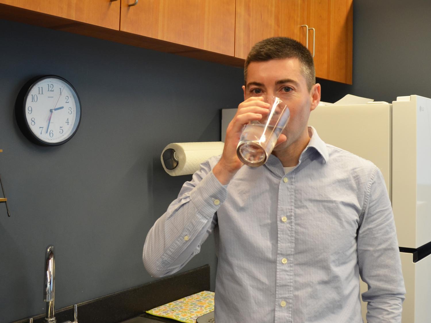 Asher Rosinger standing in a kitchen and drinking a glass of tap water