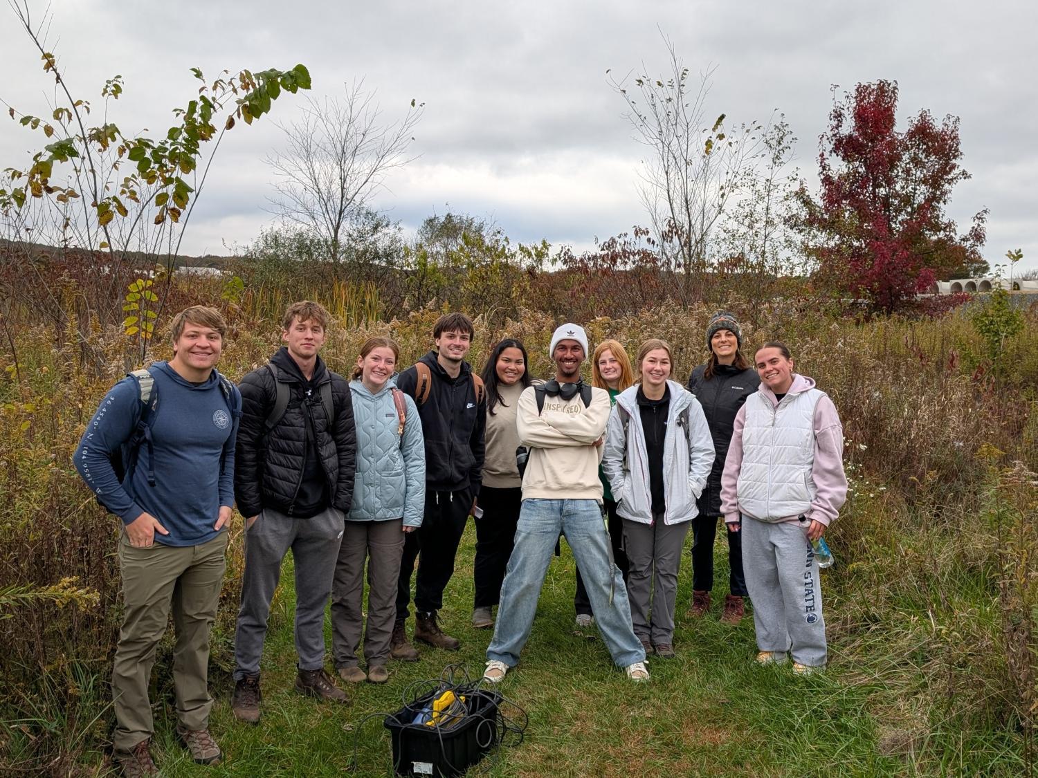 A group of students stand outside facing the camera in a field.