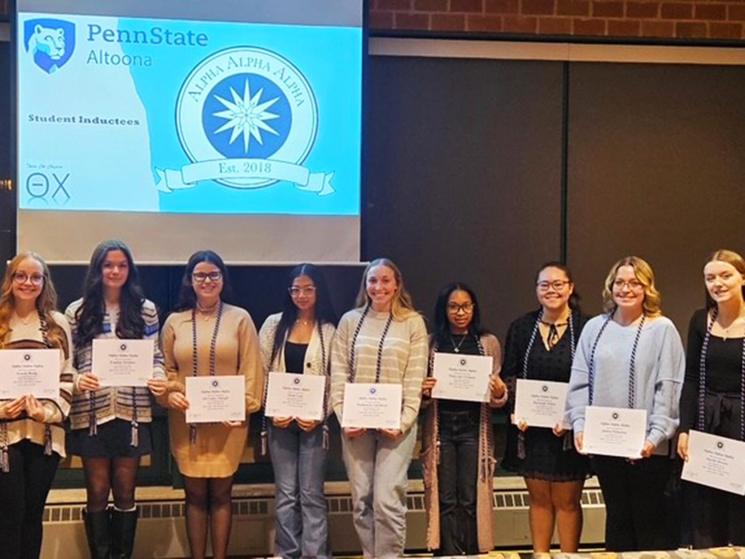A group of Penn State Altoona students stand in a row holding certificates during the Tri-Alpha Honor Society induction ceremony.
