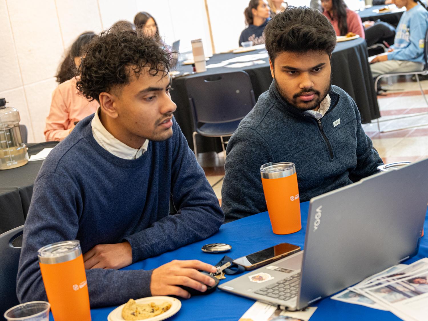 Two students look at a laptop during a luncheon