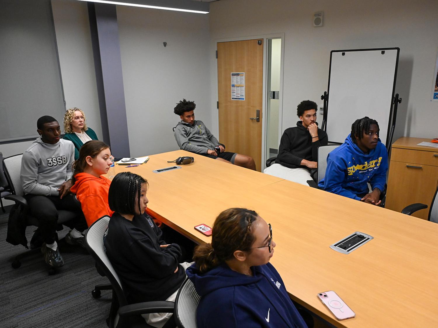 A group of students and an adviser sit around a long table listening to a presentation