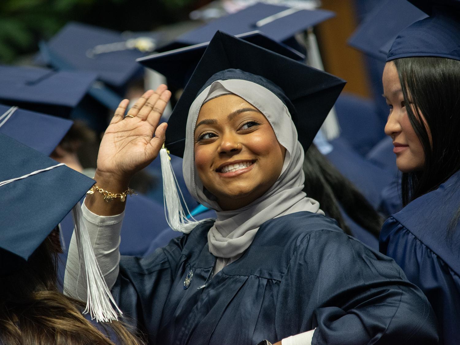 A graduate smiles and waves to the crowd
