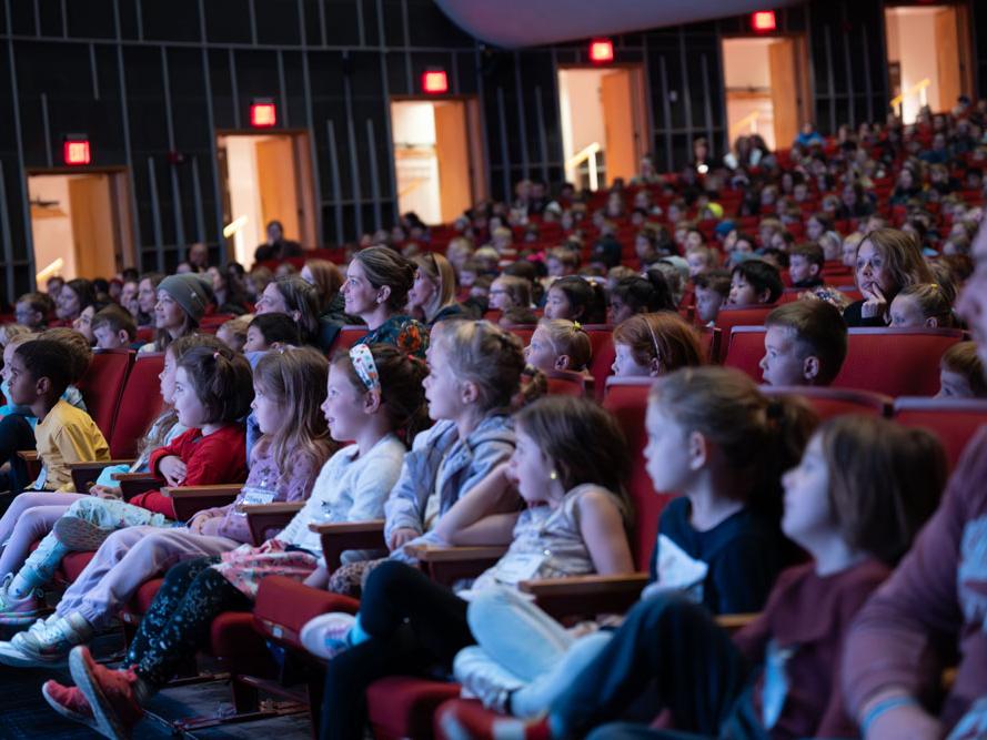 Elementary school kids sit in seats in an auditorium.