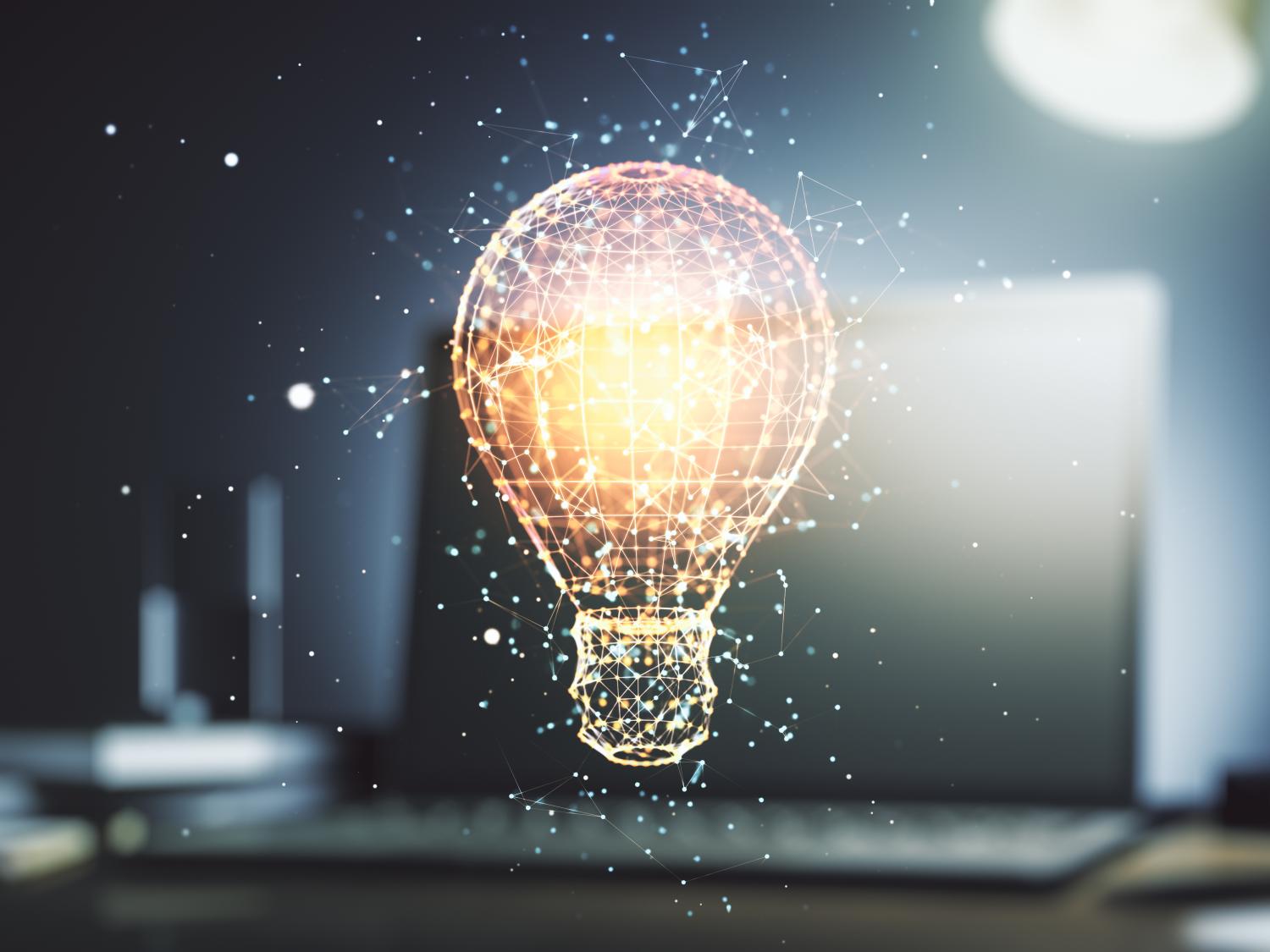 Golden glowing lightbulb atop a blurred-out laptop.