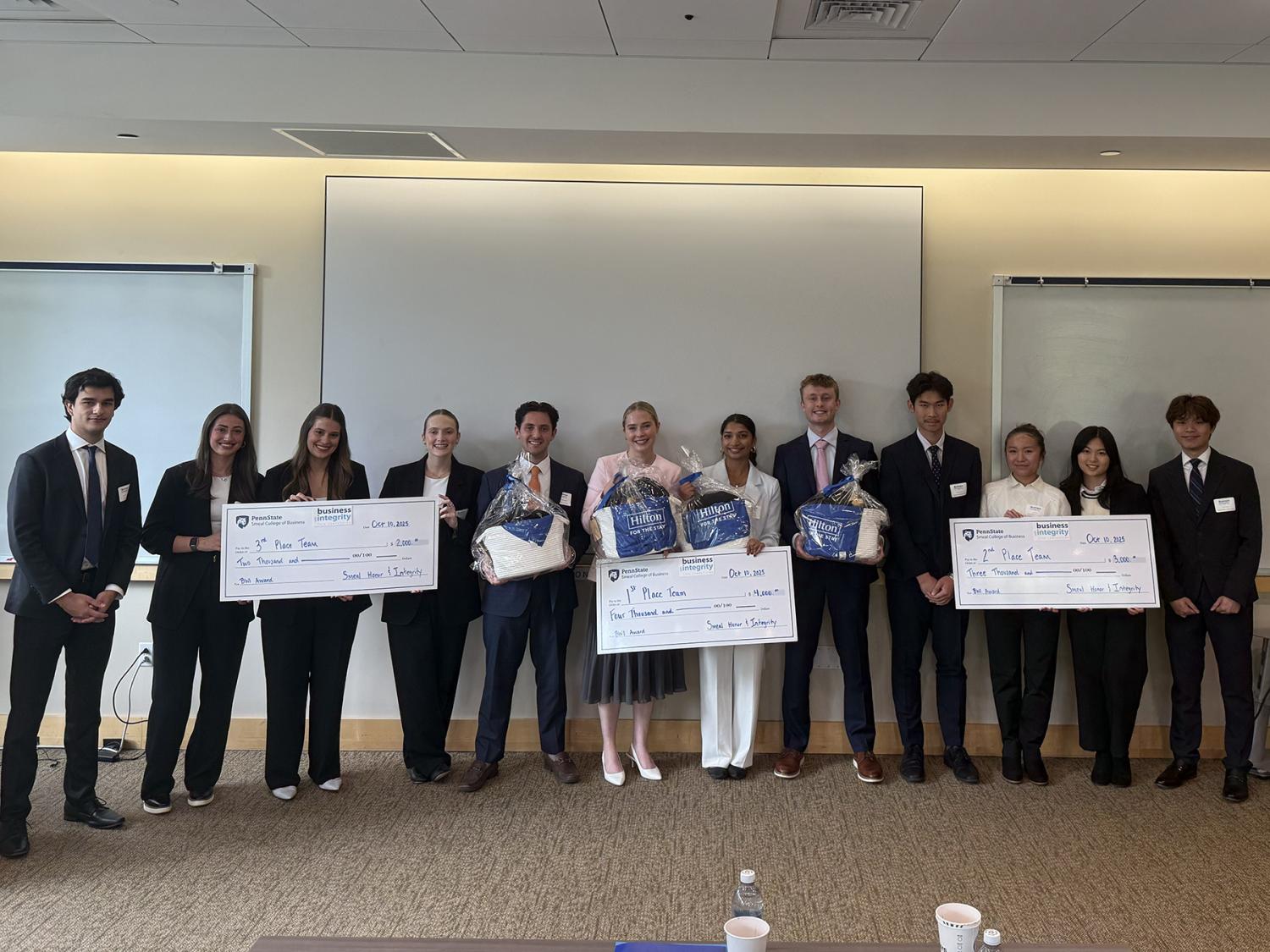 12 students dressed in business attire, some holding oversized checks, pose in front of a conference
