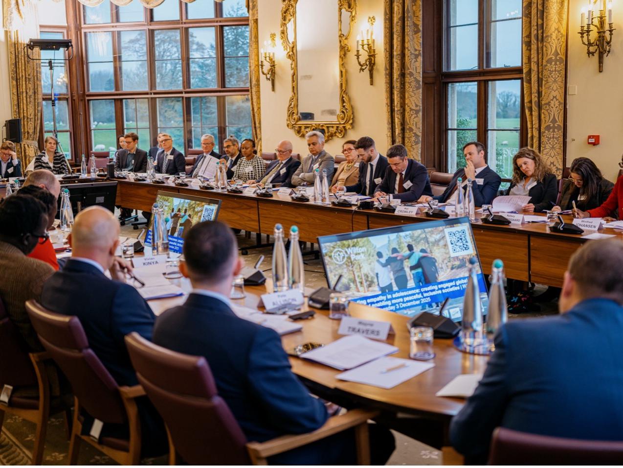 A large group of people in a roundtable meeting at Wilton Park. 