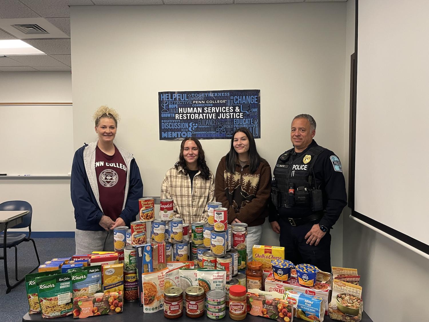 A group of four people stand behind a table filled with food donations.