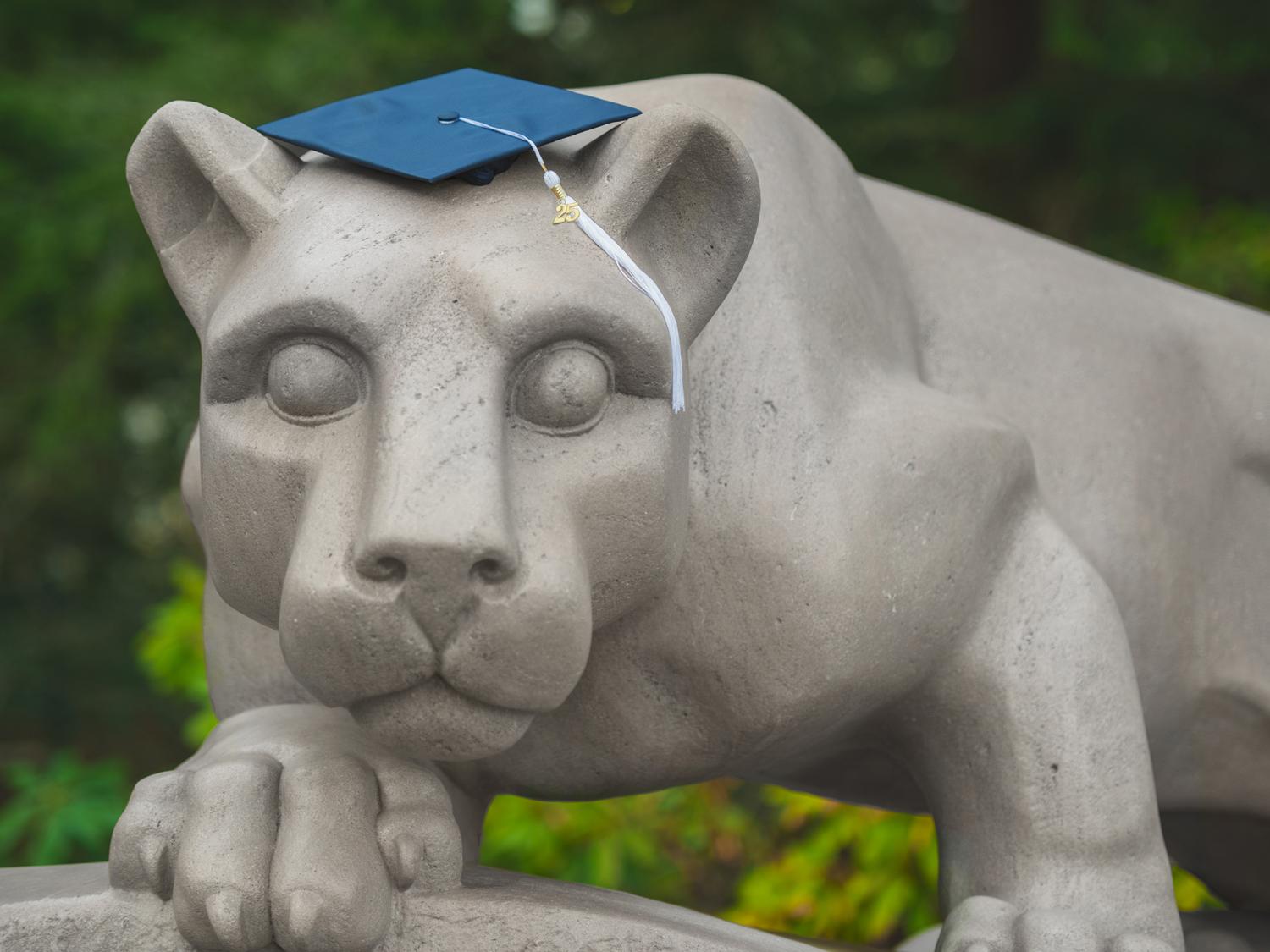 A blue graduation cap sits on top of the Nittany Lion Shrine at Penn State University Park.
