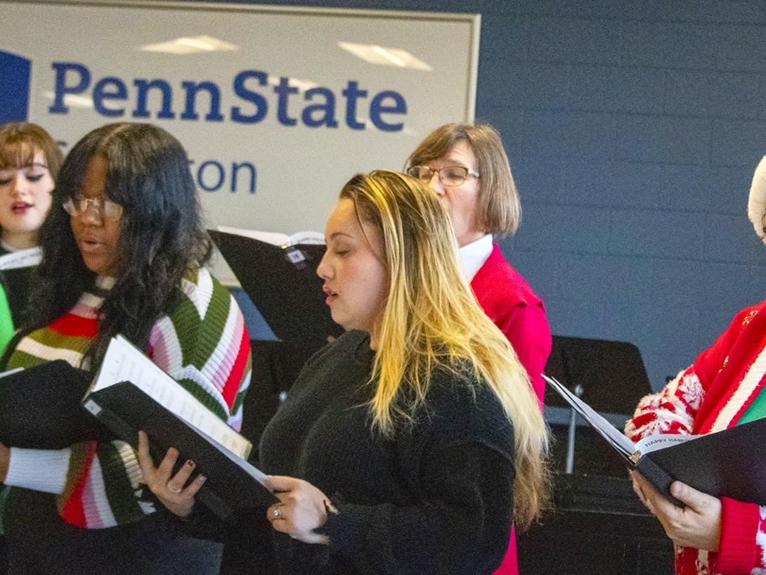 group of women holding music books and singing, dressed in holiday attire