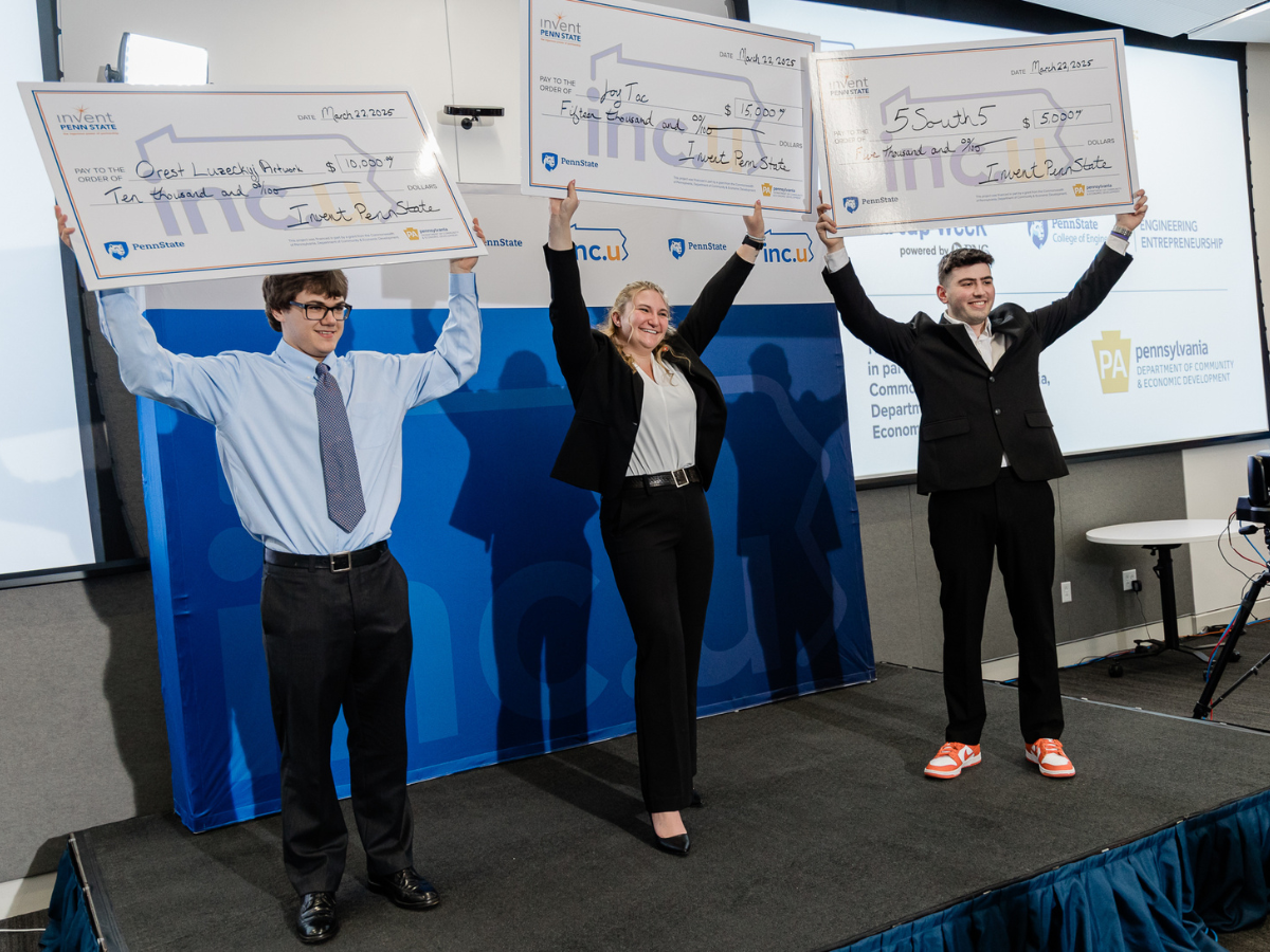Three students stand on a stage in formal attire holding up oversized checks over the heads