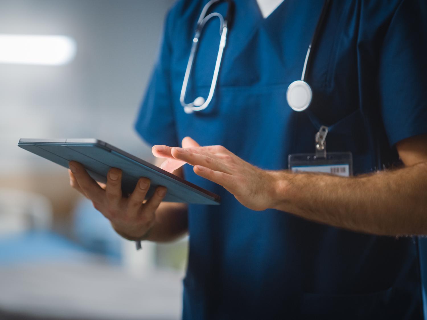 Medical professional's mid-section with a stethoscope around neck typing on iPad.