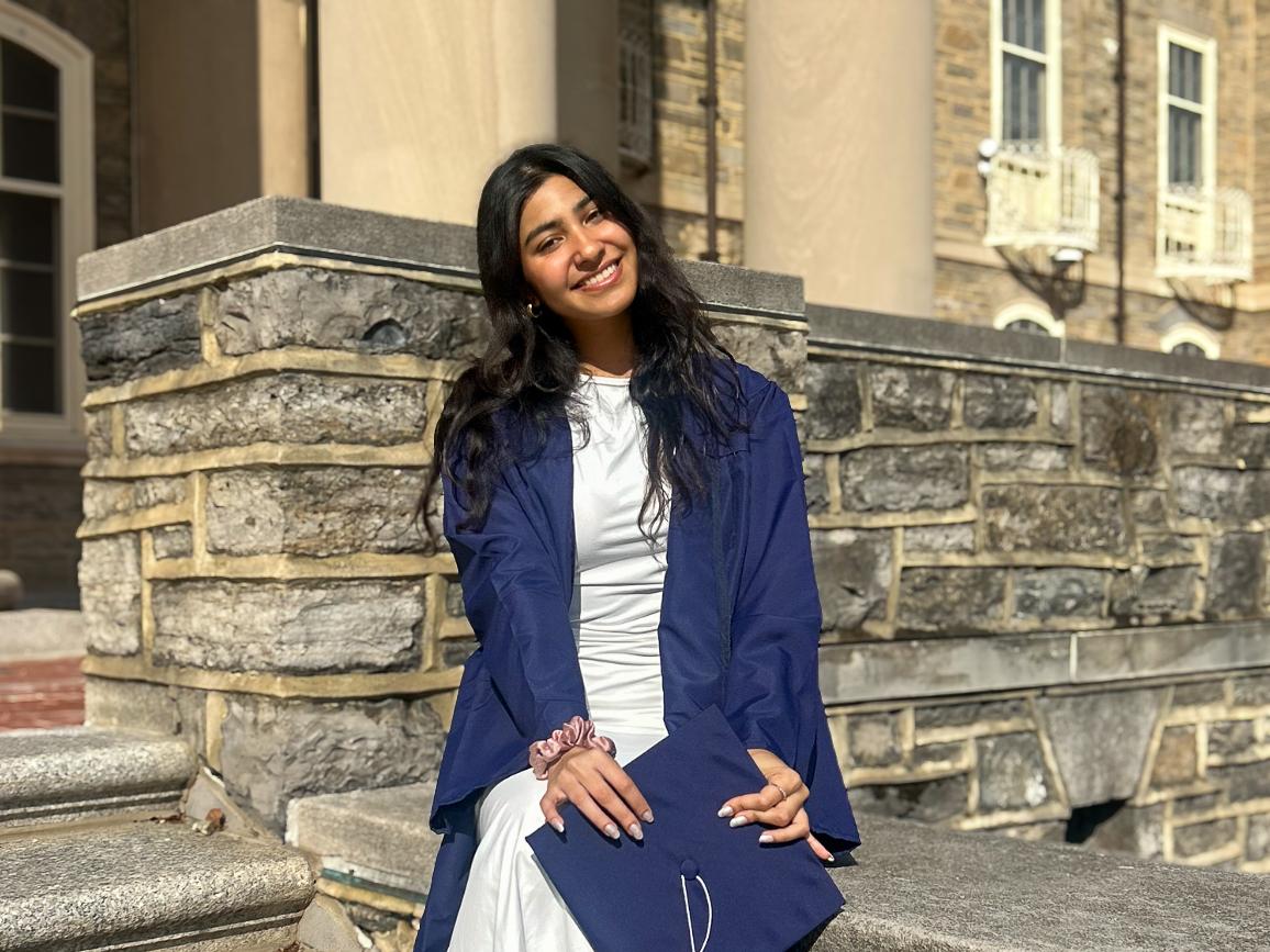 Vama Maniar sits in a graduation cap and gown on the steps of Old Main.