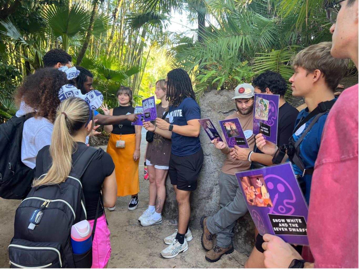 A group of Penn State New Kensington students stand together in a wooded area at Disney’s Animal Kingdom, holding printed cards and discussing design concepts as part of an engineering-focused workshop.