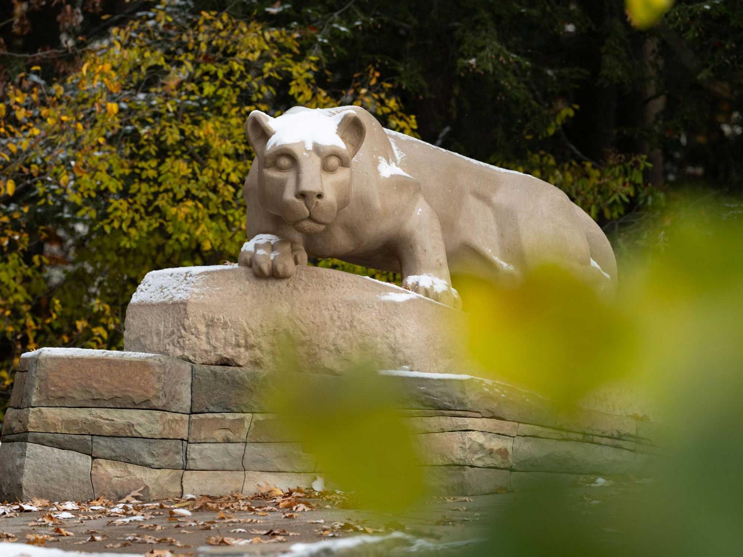 The Nittany Lion Shrine, framed by green bushes and trees, with a fresh coating of new snow.