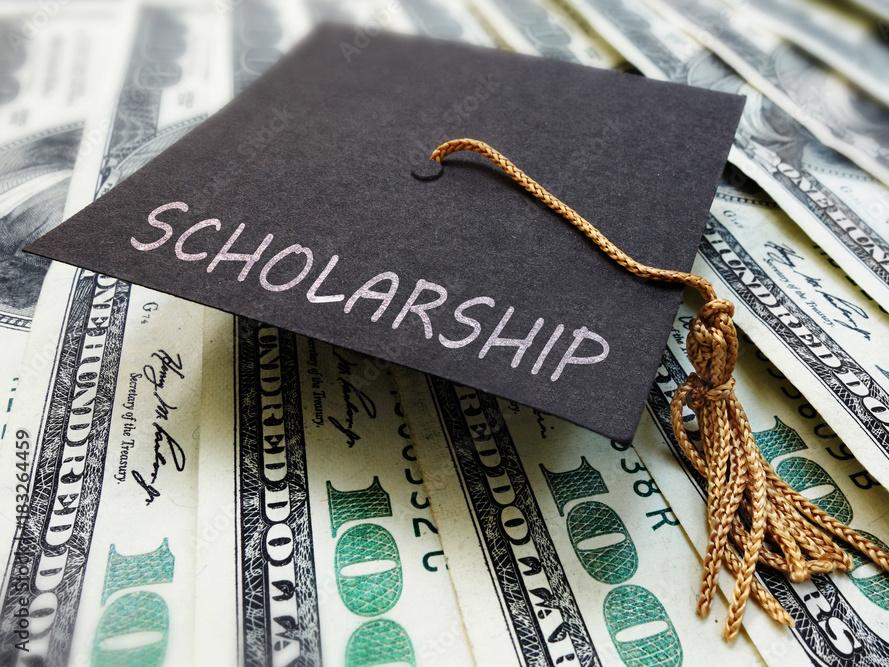 graduation cap with word scholarship on brim atop display of hundred dollar bills