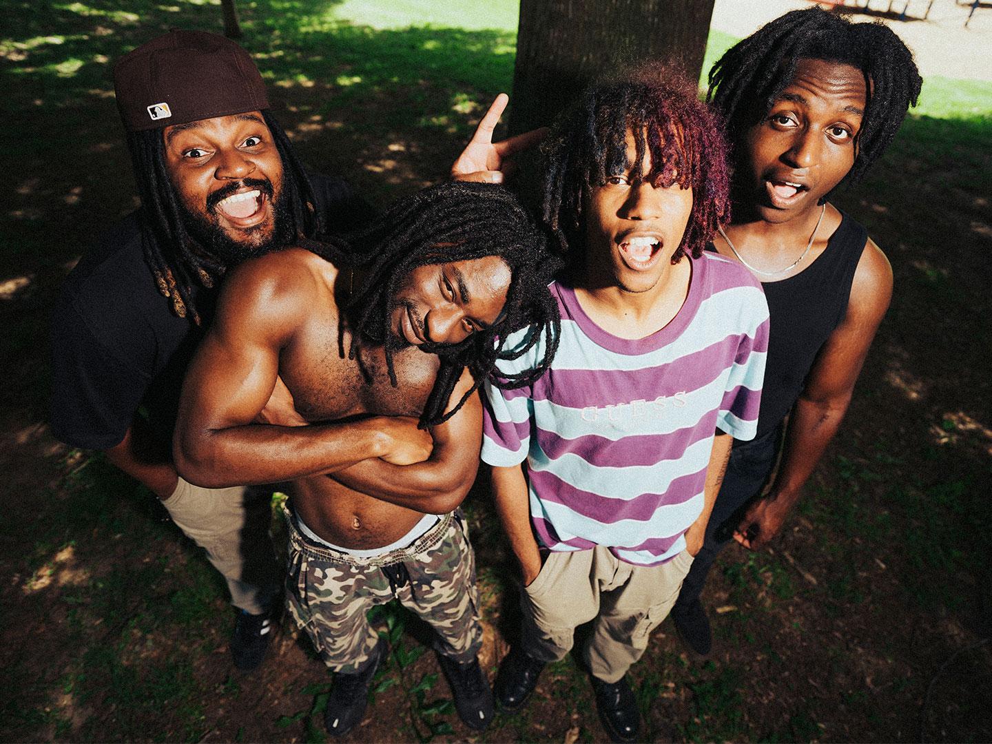Four Black men with dreadlocks make silly faces for the camera.