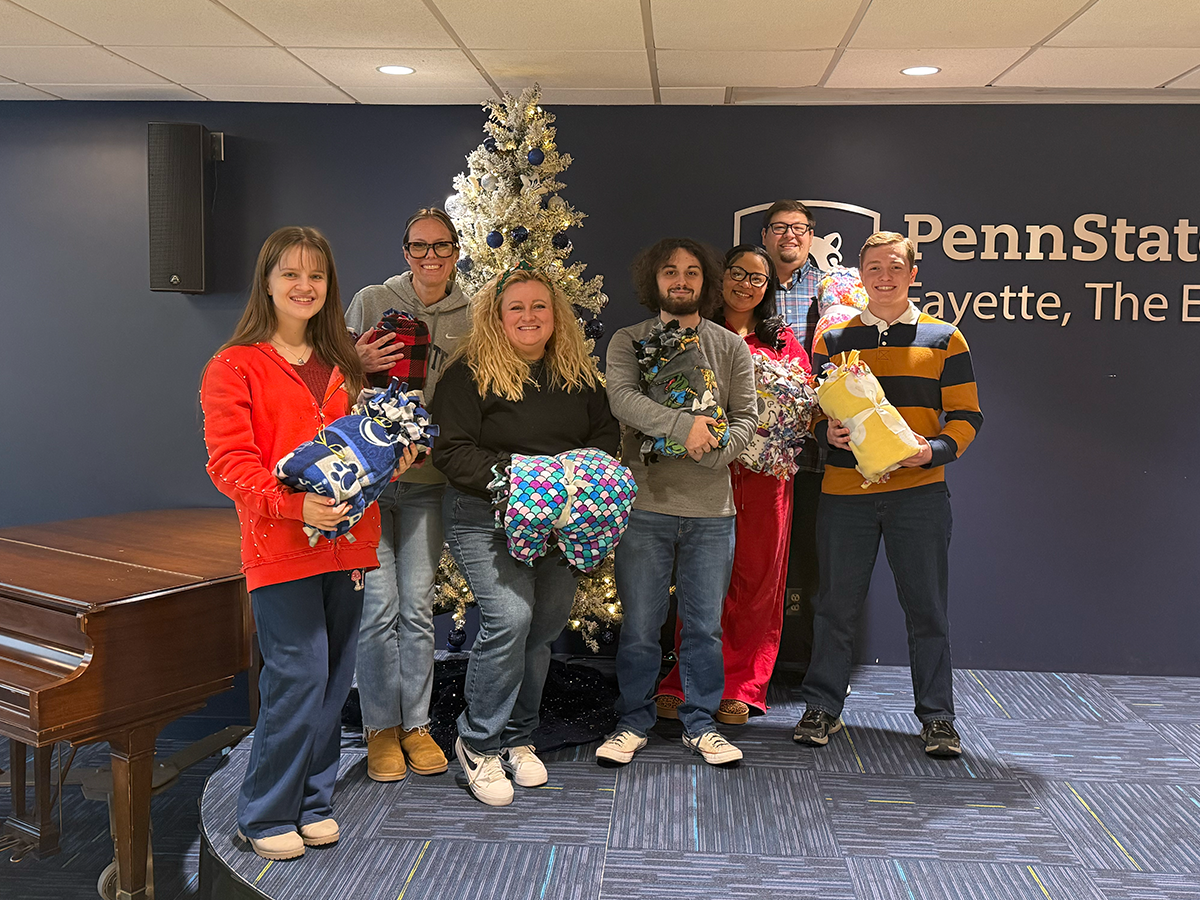 A group of Penn State Fayette students and Student Affairs staff stand together behind a table displaying 35 completed fleece blankets.