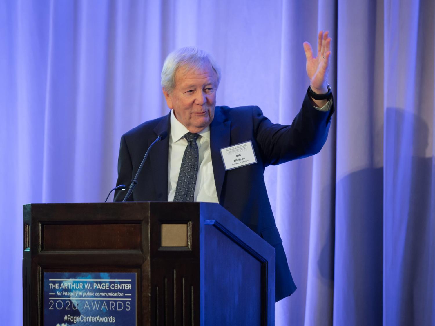 A man in a suit speaks to a crowd at a podium. 